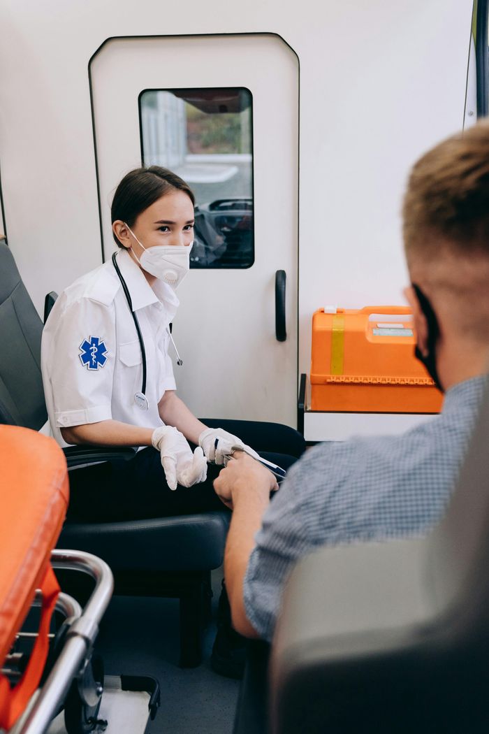 gallery-04 A paramedic wearing a mask assists a patient inside an ambulance, ensuring safety and care.